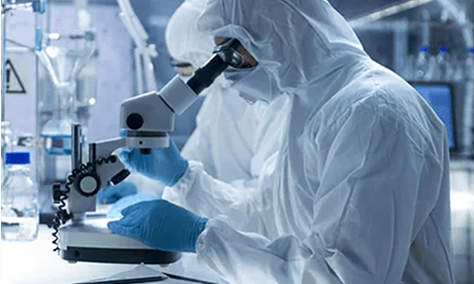 A scientist in a cleanroom looks through a microscope